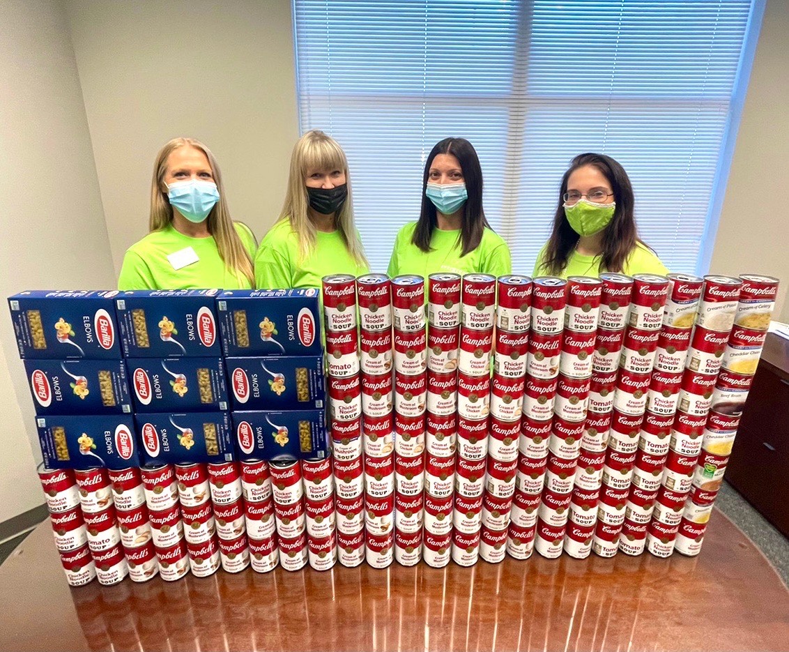 image of four masked women behind a large stack of canned soup and boxes of pasta arranged in the shape of the US flag