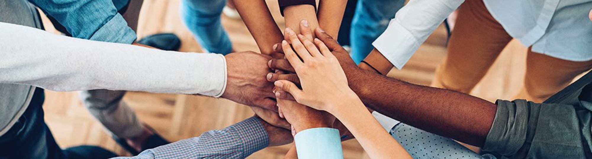 individuals of all colors join hands in a huddle 